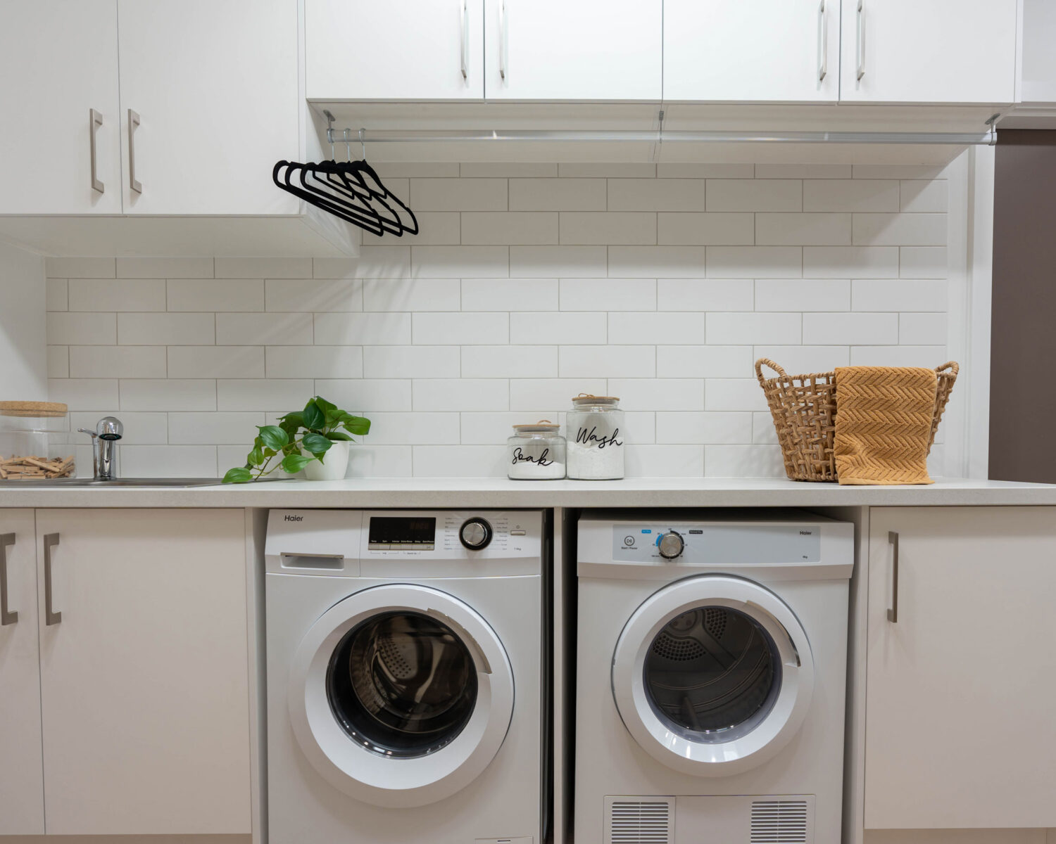 Image of a white laundry with brick bond pattern whtie subway tiles. Using a hanging rail adds functionality to the space