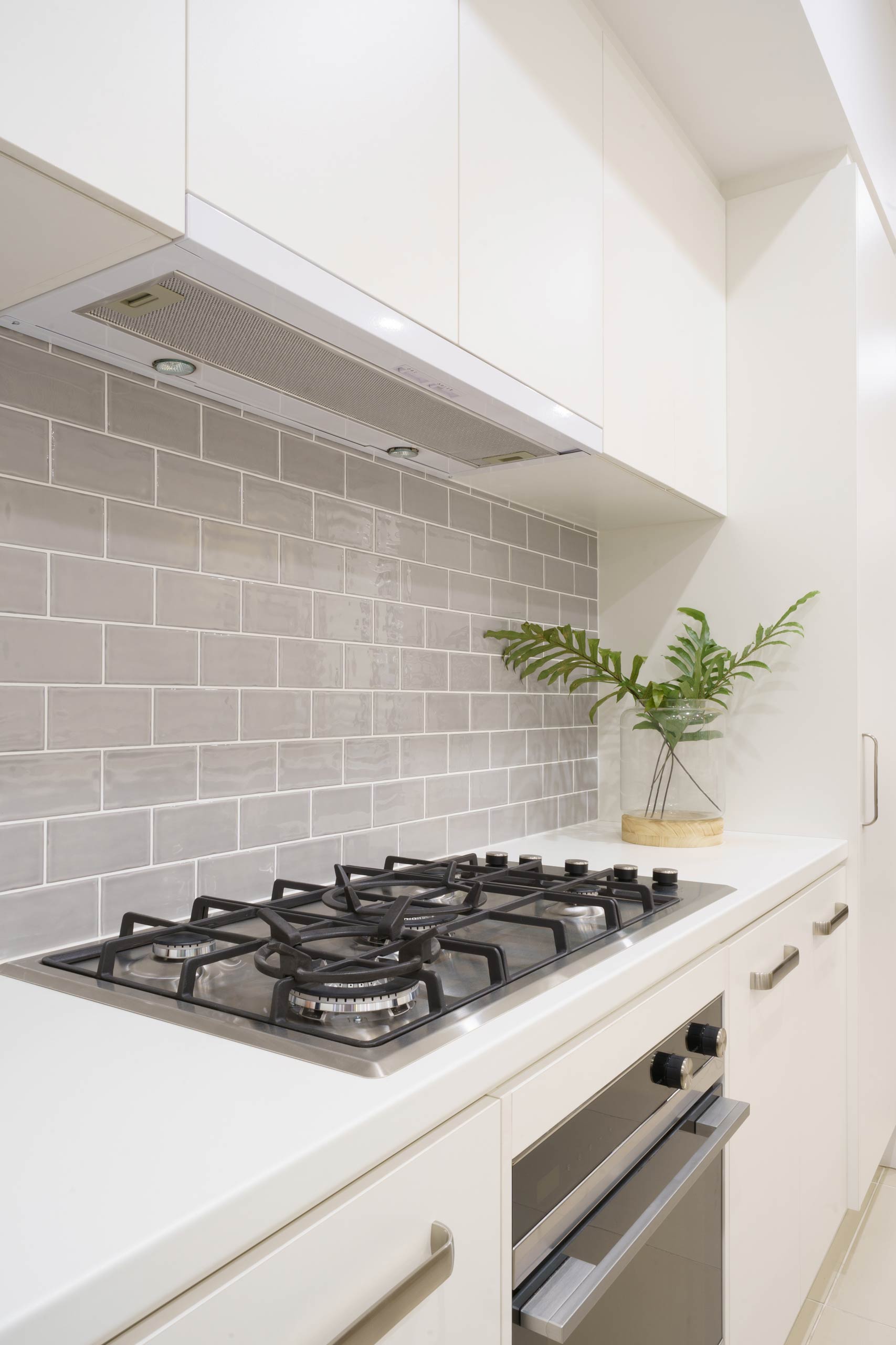 White Kitchen with grey subway tiles in brick bond pattern. Pull out undermount rangehood with gas cooktop and electric oven