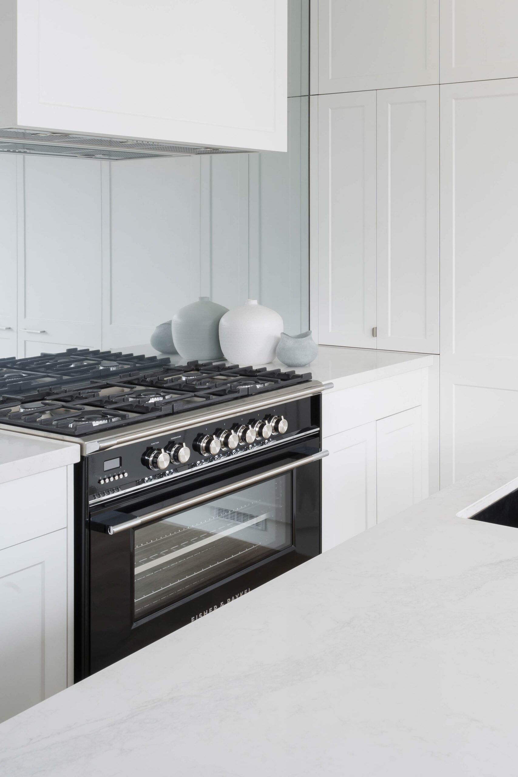 White Shaker style kitchen cabinetry with glass mirror splashback and a Fisher & Paykel freestanding black oven