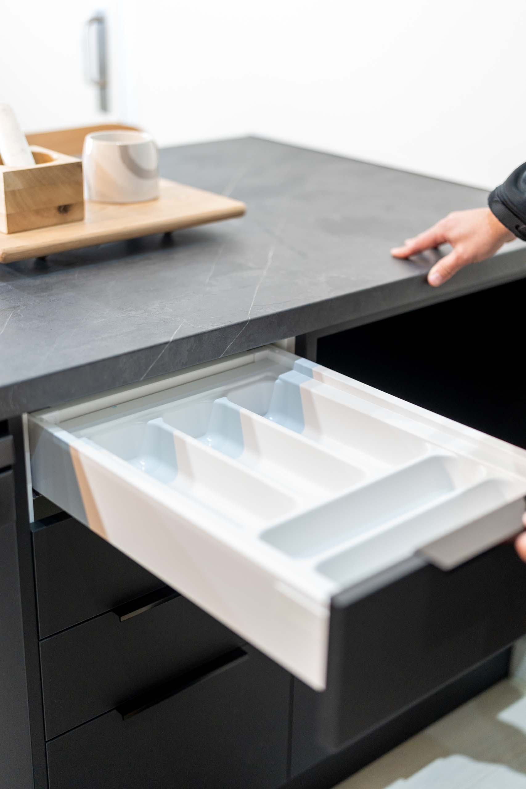 Image showing cutlery tray cabinet accessory in top drawer of drawer cabinet. Cabinetry is black with dark grey veined laminate benchtop and black lip handles.