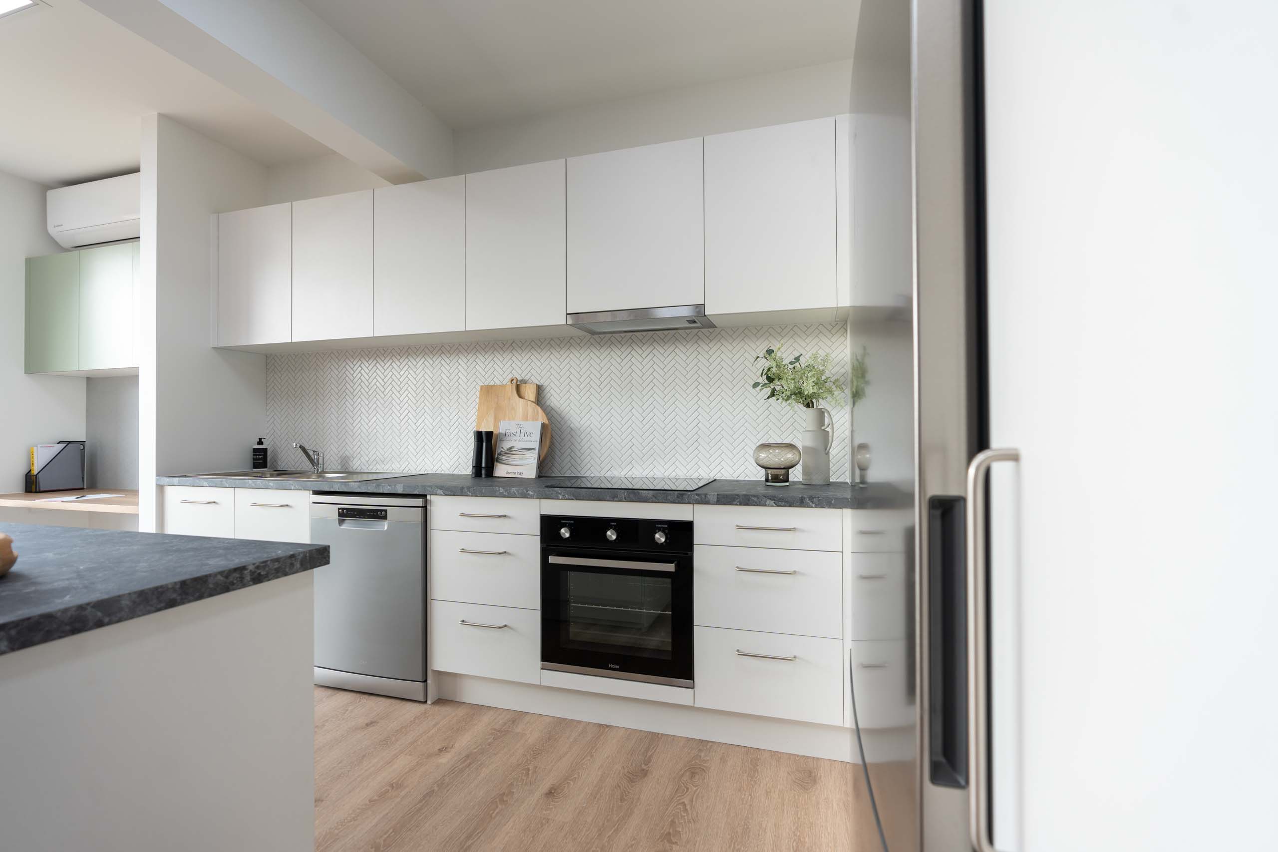 White kitchen with black veined laminate benchtop. White herringbone tile splashback