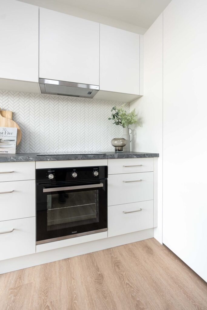 White kitchen with black veined laminate benchtop. White herringbone tile splashback