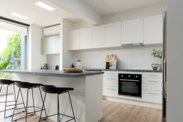 White kitchen with black veined laminate benchtop. White herringbone tile splashback.