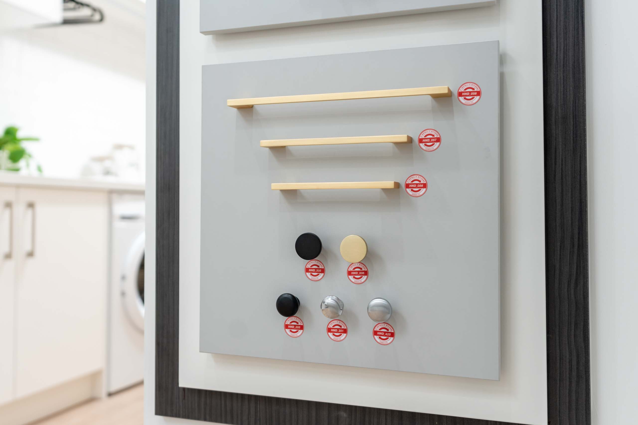 Image of a U-Install-It Kitchens showroom, in the selections room, showing a close up of one of the cabinet handle ranges available. Gold bar handles, and knob handles in black, gold, brushed chrome, and shiny chrome.