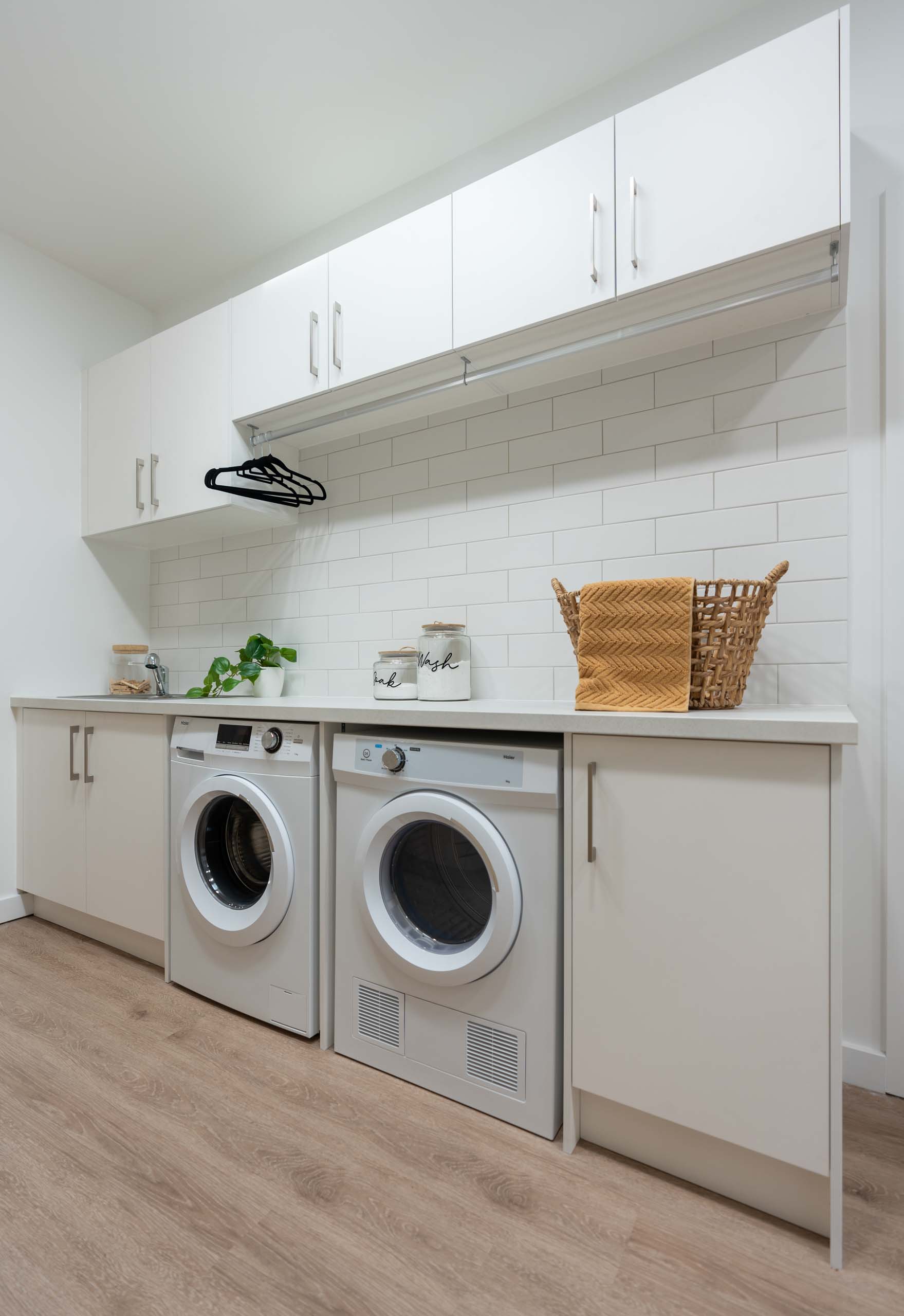 White laundry with overhead cabinets showcasing a hanging rail. White subway tiles in a brick bond pattern