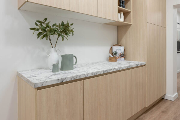 Butlers pantry in light timber grain cabinetry with a laminate benchtop in a marble look design, Overhead cabinets with an open shelf display unit