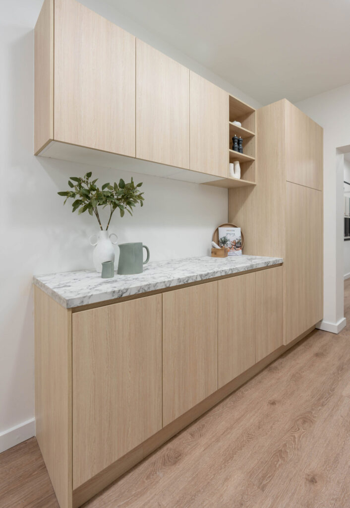Butlers pantry in light timber grain cabinetry with a laminate benchtop in a marble look design, Overhead cabinets with an open shelf display unit