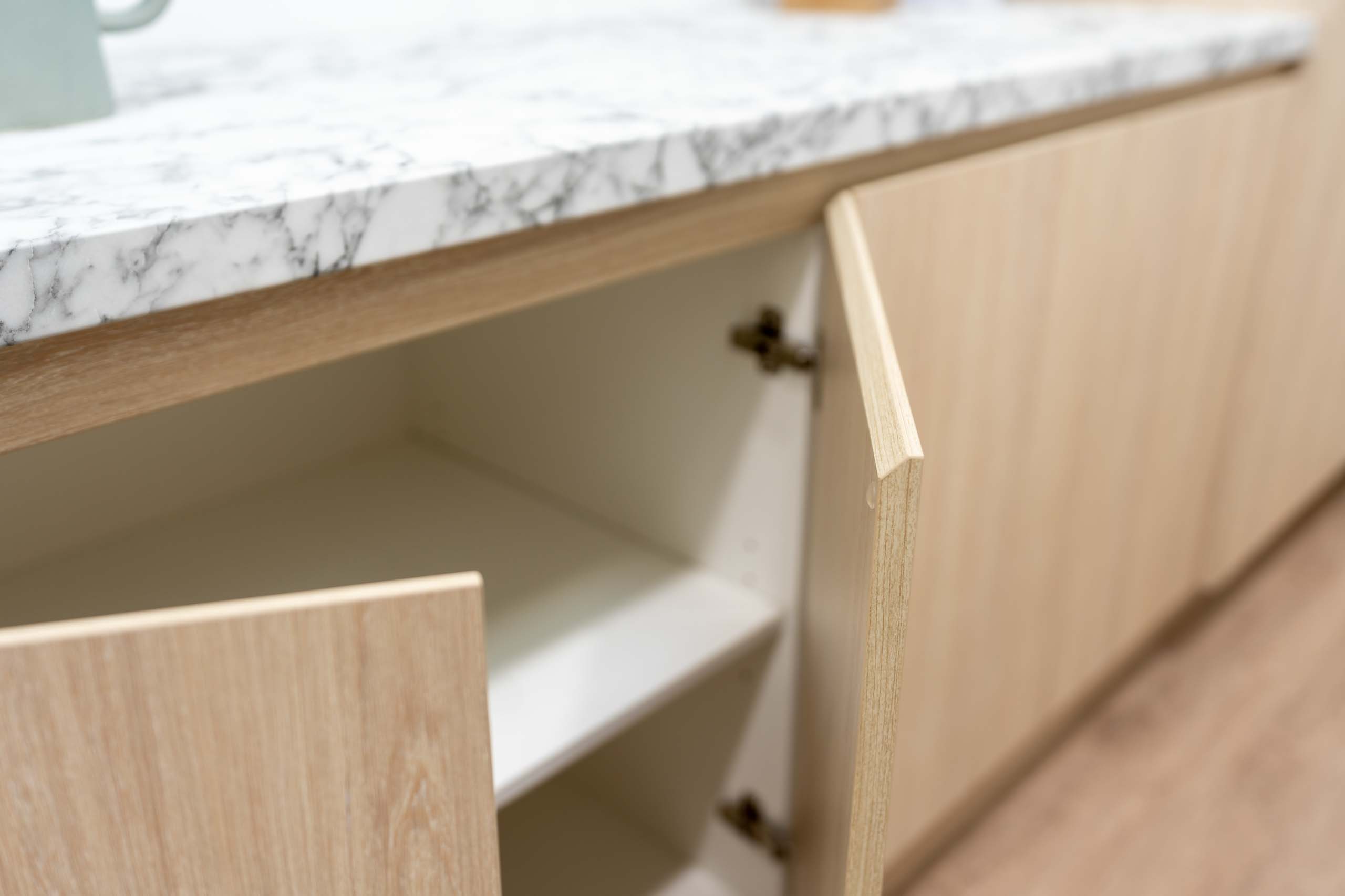 Image showing K-handle finger grip cabinet handle solution, with light timber grain cabinetry and marble look laminate benchtop.