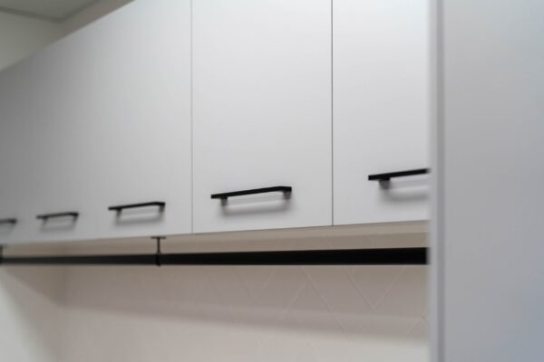 Black hanging rail in a laundry with white cabinets and black handles